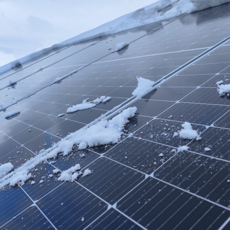 A bit of snow and ice covering solar panels on the roof of a house